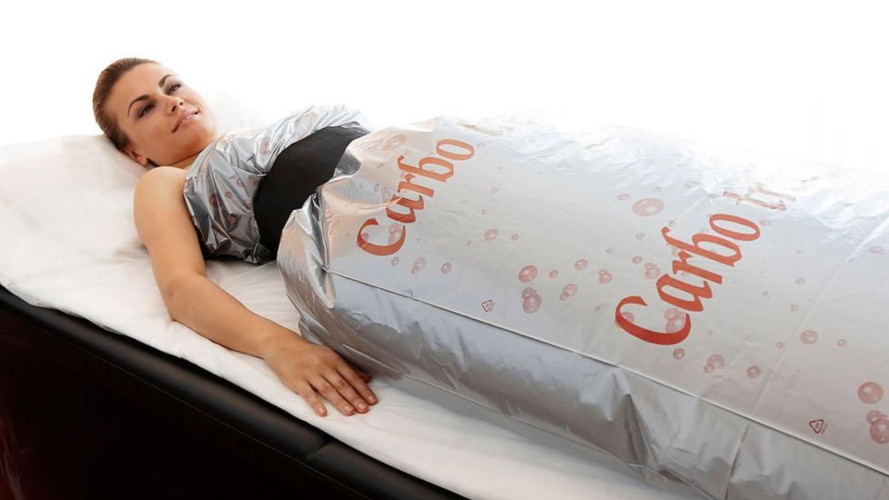 Ženska leži na postelji, zavita v srebrno prevleko z napisom